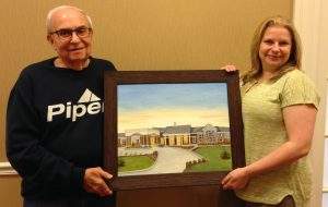 Gary Stahl presents his panting, "Our New Home" to Amy Watson, life enrichment director.