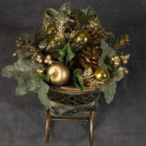 Christmas Forever - Detail image of sleigh basket with gold Christmas ornaments and pinecones finished off with green bow