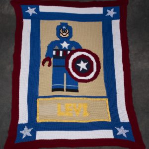 Fiber Arts - Captain America - Crochet afghan in red, white and blue yarn. White stars in each of the four corners frame the image of a lego sytle figure of Captain Ameria.