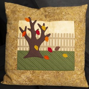 Fiber Arts - Falling Leaves - Pillow with fabric and felt material featuring a brown tree trunk with red, orange, brown and yellow leaving falling off of it.