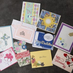 Mixed Media Crafts - Card Collection - Image of 10 hand made cards featuring intricate cut outs of leaves, flowers, hearts, butterflies and Christmas images that adorn each card.