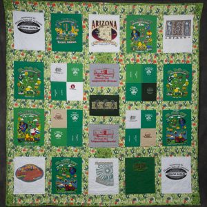 Quilting - Arizona Retirement Adventures - quilt with a desert cactus fabric background with squares on top of fabric made from various t-shirt swatches from their adventures.