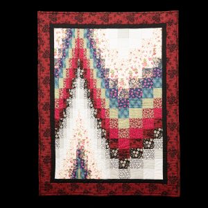 Quilting - Bargello Study - quilt made of various colored patterned fabrics of red, purple, pink, black, beige and white where strips of fabric are sewn together to form a tube, the tubes are cut into various widths and sewen together to make stairstep patterns.