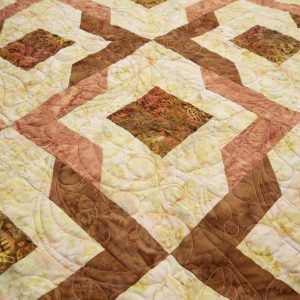 Quilting - Butterscotch Delight - Detail - quilt of various V and square shaped patterned fabrics in colors of orange, brown, gold and peachen patterned fabrics placed side to side that creates unique rows of design.