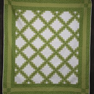 Quilting - Irish Chain - quilt made of various patterned green fabrics with white accents. Rows of white staristep style blocks form eight rows of alternating blocks of white that are separated by crisscross diagional rows of smaller solid green and green plaid blocks.