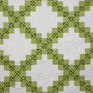 Quilting - Irish Chain - Detail - quilt made of various patterned green fabrics with white accents. Rows of white staristep style blocks form eight rows of alternating blocks of white that are separated by crisscross diagional rows of smaller solid green and green plaid blocks