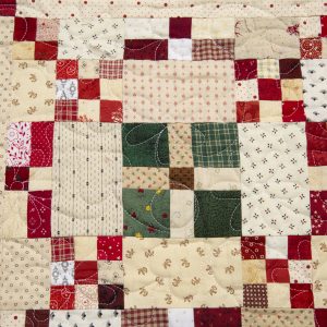 Quilting - Merry Merry Christmas Throw - Detail - quilt made from small fabric blocks of patterned red, green, beige and white designed in a motif with twelve circle shapes all connected with small blocks giving a crisscross effect.