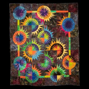 Quilting - Total Eclipse - quilt with muted background colored patterned fabrics in shades of mauve, blue, brown and gold with vibrant colors of yellow, orange, green, red, purple and blue shaped as triangles and pieced together to create 13 circular shapes that appear to be bright sunbursts.