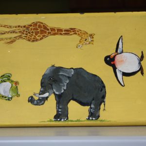 Sculpture 3D - Animal Stool - small step stool painted a yellow color with a variety of animals painited on it. The top of the stool features a painted green frog with red eyes, a large gray elephant with tusks, a balck and white penguin and a golden giraffe.