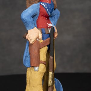 Sculpture 3D - Annie Smokely - Detail - sculpture of a lady with brown hair smoking a cigarette with a rifle in front of her and her hand on a pistol that is in her holster on her hips. The lady is wearing brown boots with a colorful target leaning against her leg.