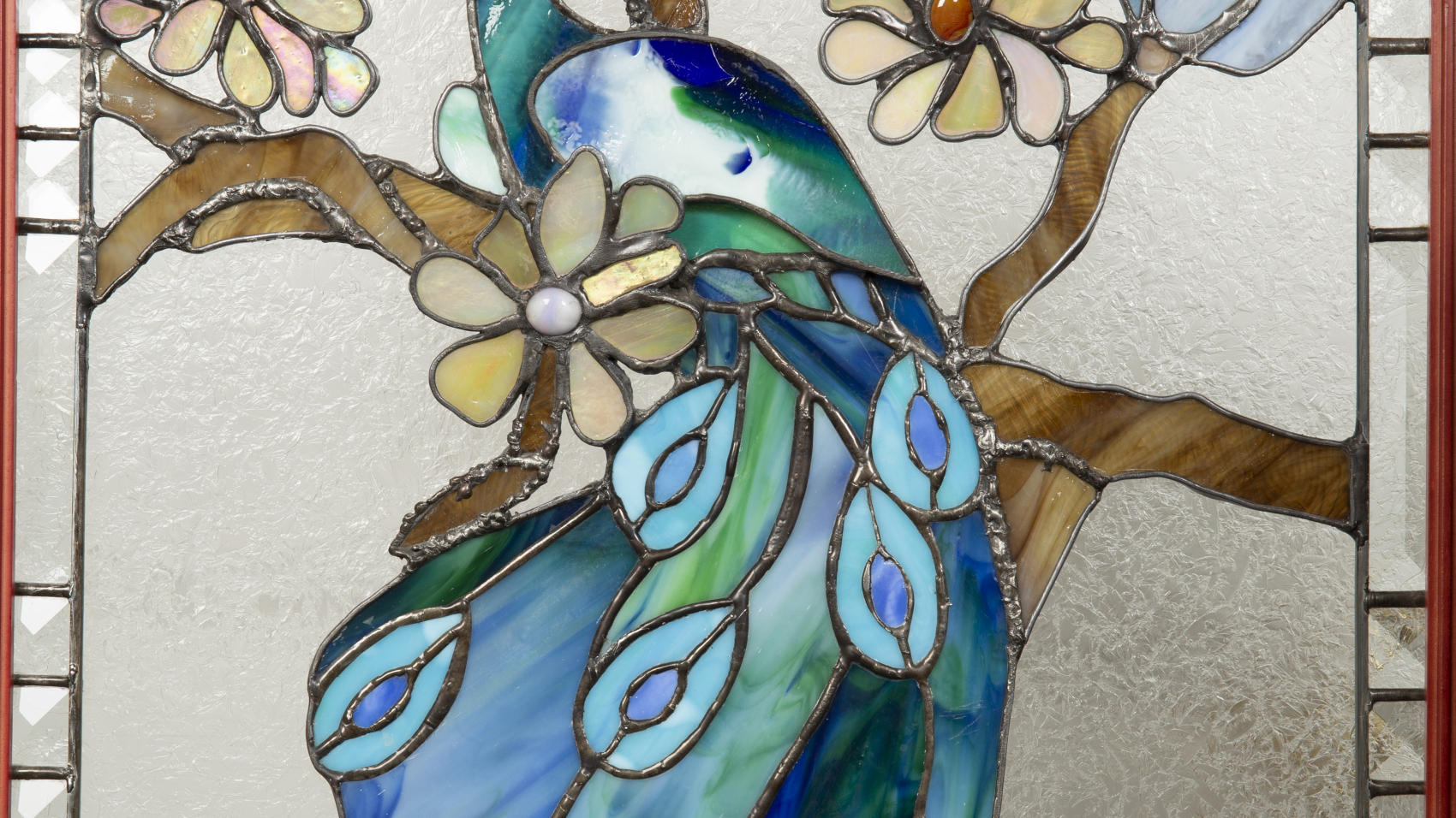 Sculpture 3D - Jasper the Peacock - image of a stained glass peacock in shades of blue on a brown branch with beige and blue flowers.